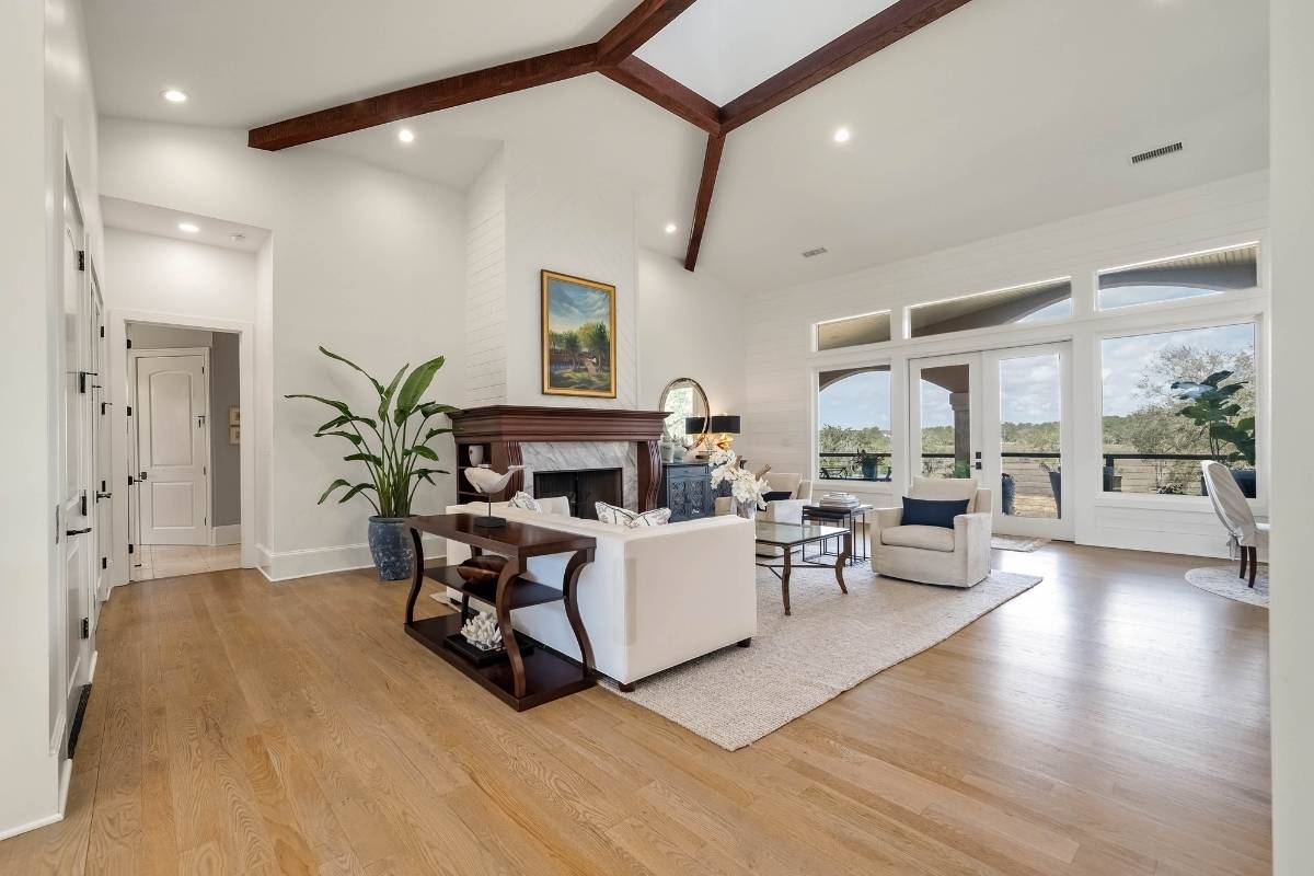 Great room with vaulted ceiling, exposed wood beams, wood-burning fireplace, and French doors to covered porch at 6411 China Back Lane, Meggett SC