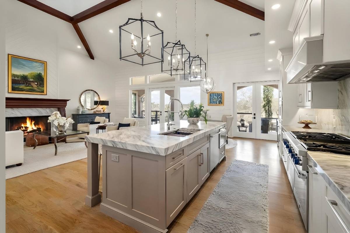 Open-plan gourmet kitchen and great room with vaulted ceiling, wood beams, marble island, and wood-burning fireplace at 6411 China Back Lane, Meggett SC