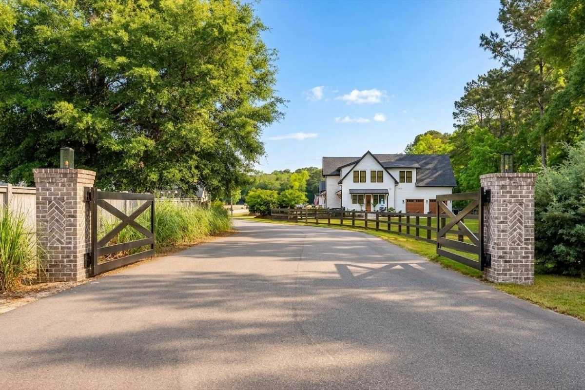 Gated entrance to Haven Estates on Johns Island SC with wooden cross-buck gates, brick columns, and a modern farmhouse home beyond