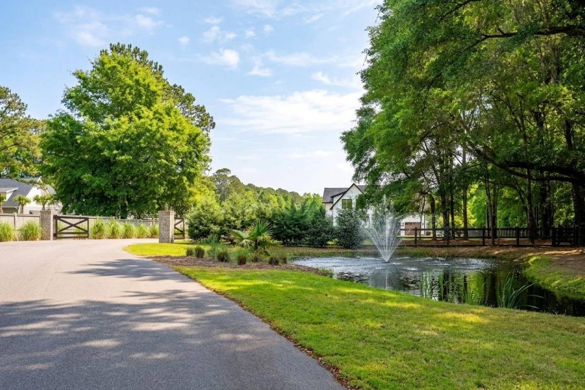 Tree-lined street inside Haven Estates Johns Island with a pond fountain, neighborhood gate, and modern farmhouse home surrounded by Lowcountry landscaping