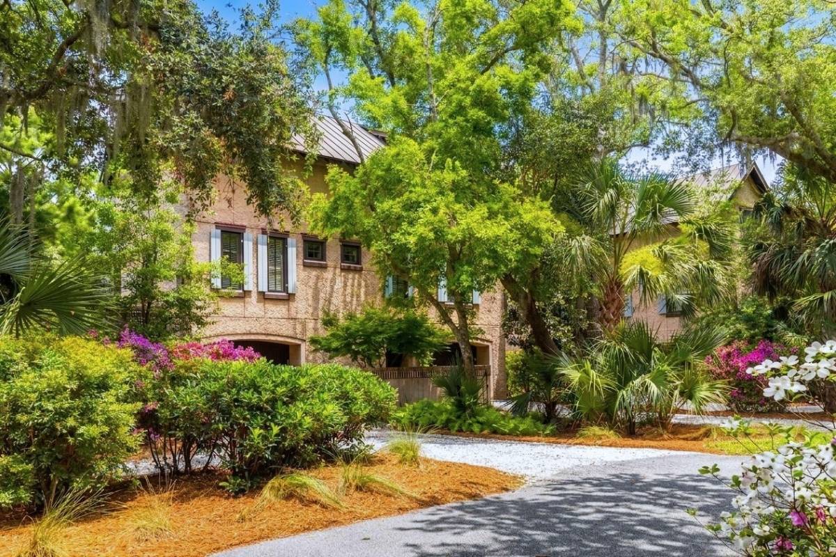 Cypress Point cottage exterior with stucco facade, blue shutters, and blooming azaleas in East Beach Village, Kiawah Island