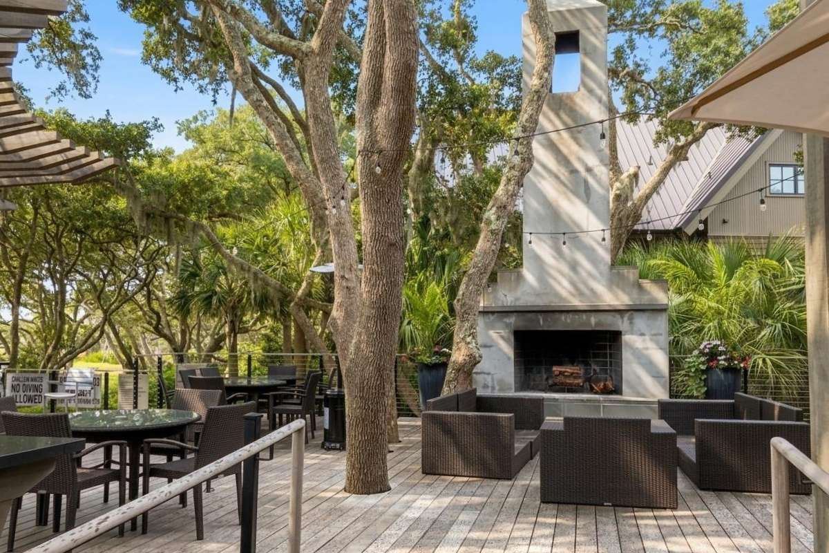 Marsh House outdoor deck with fireplace, string lights, and live oak canopy at Ocean Park, Kiawah Island