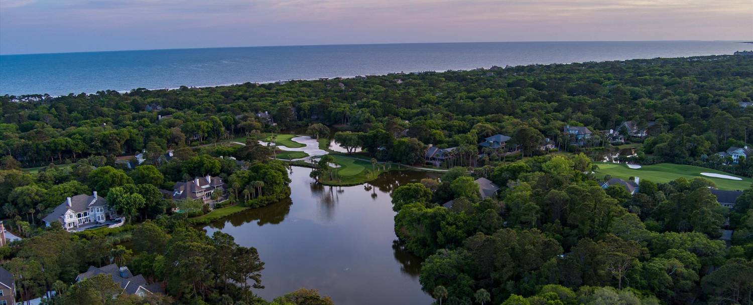 Aerial view of Kiawah Island luxury homes and golf course fairways set among maritime forest with the Atlantic Ocean in the background
