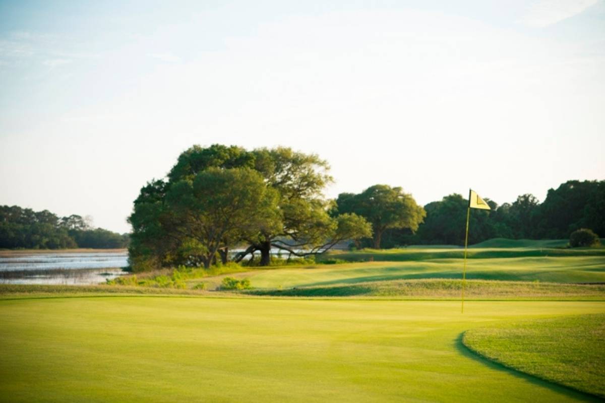 Golf course green with flag and tidal creek bordered by live oaks at Oak Point golf course, Kiawah River Estates, Johns Island SC