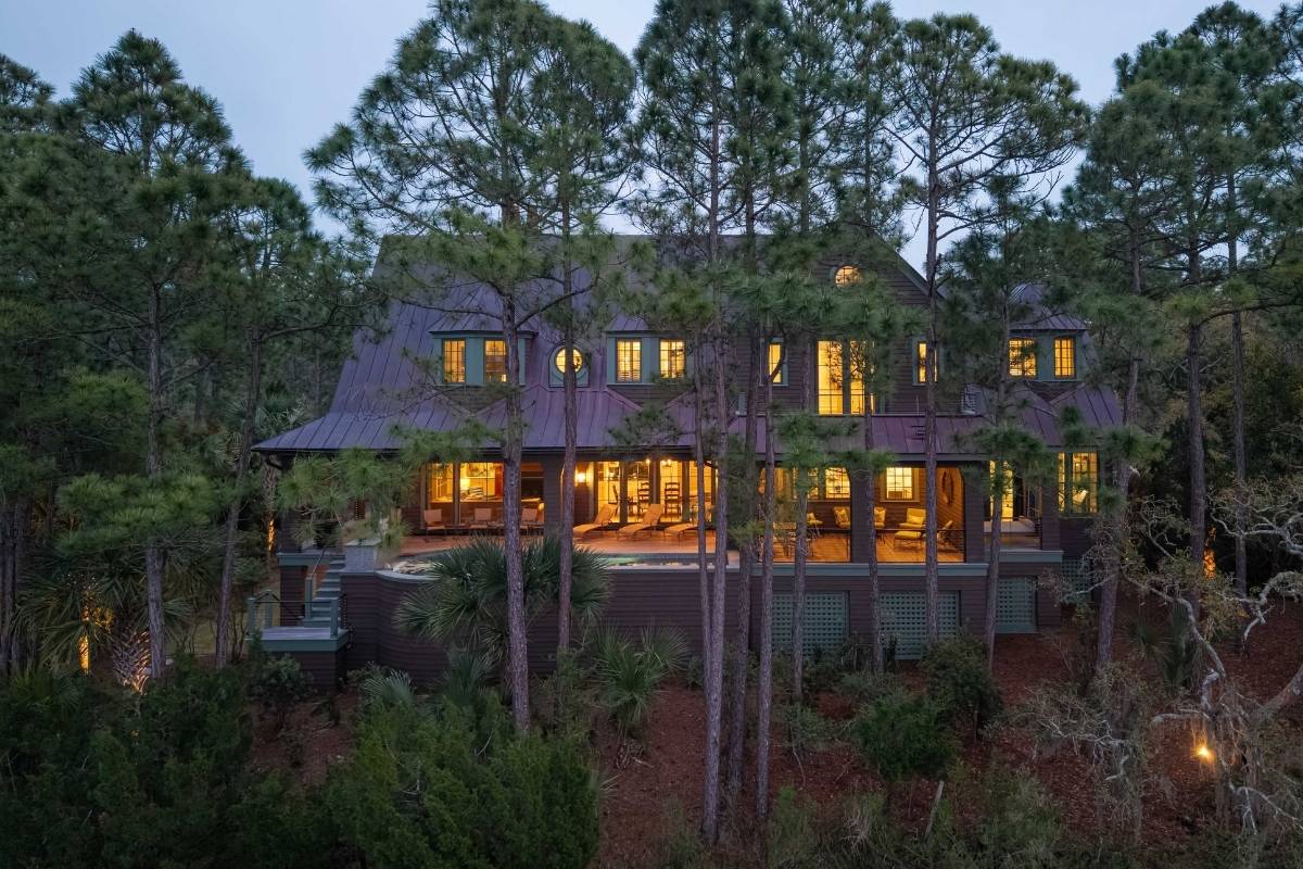 Large luxury home lit from within at dusk surrounded by tall pines and palmetto trees in The Preserve, Kiawah Island SC