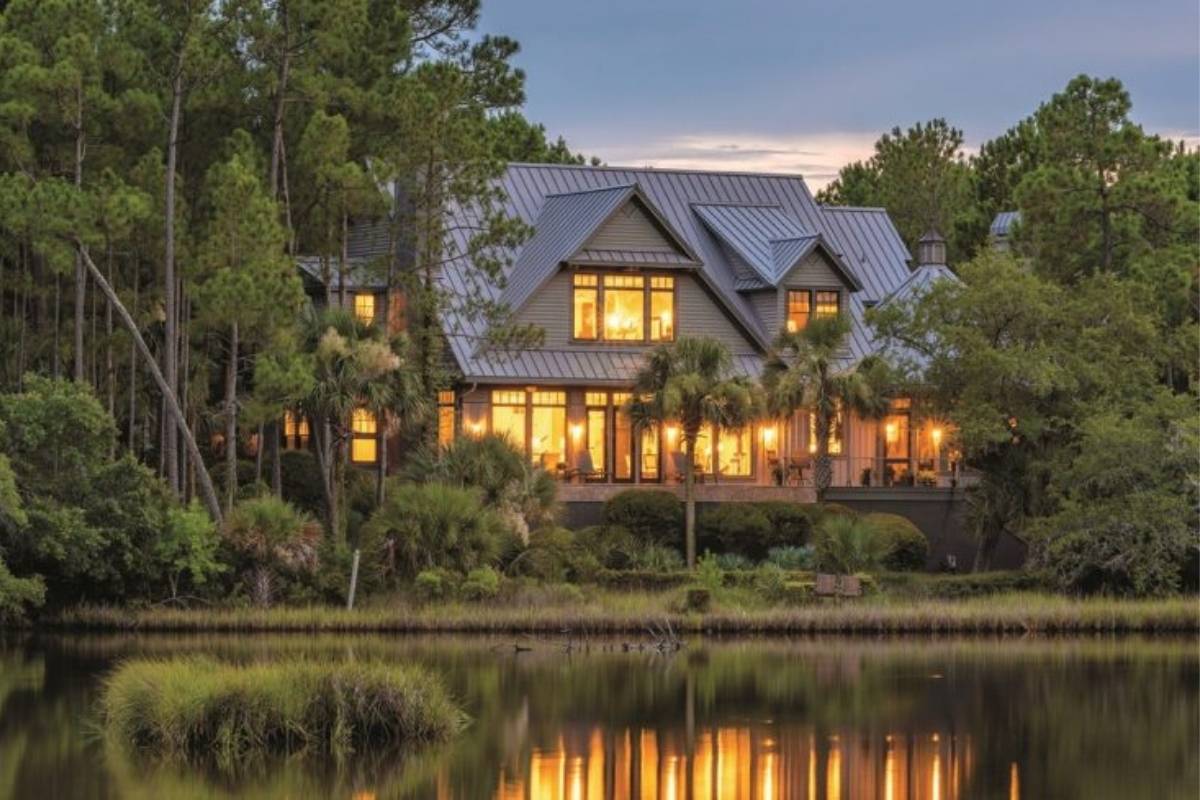 Lowcountry home with metal roof reflected in lagoon at dusk, surrounded by pine trees and palmettos in The Preserve, Kiawah Island SC