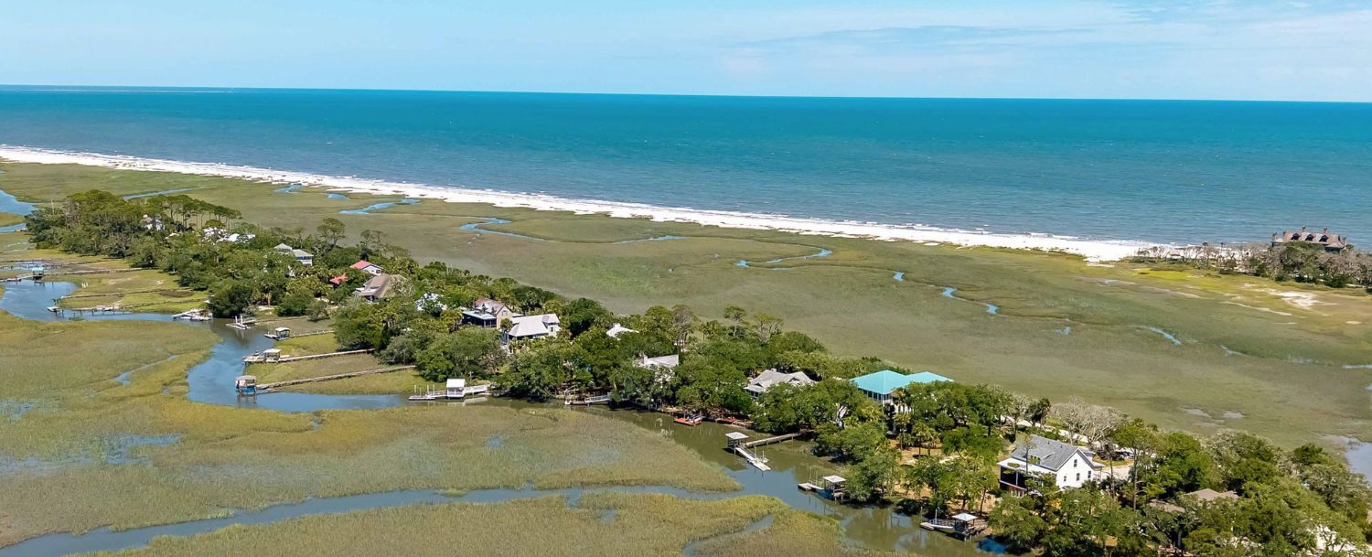 Aerial view of Edisto Island showing marsh waterways, wooded homesites with private docks, and the Atlantic Ocean beyond