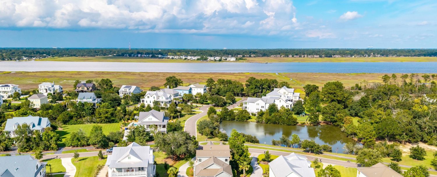 Aerial view of Rushland Landing on Johns Island, SC, showing custom Lowcountry homes, a freshwater lagoon, and the Stono River marsh beyond